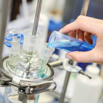 A hand fills a turquoise blue liquid into another glass vessel in the laboratory.