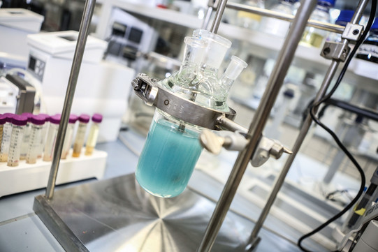 A sample vessel with light blue liquid is firmly clamped in a metal holder.
